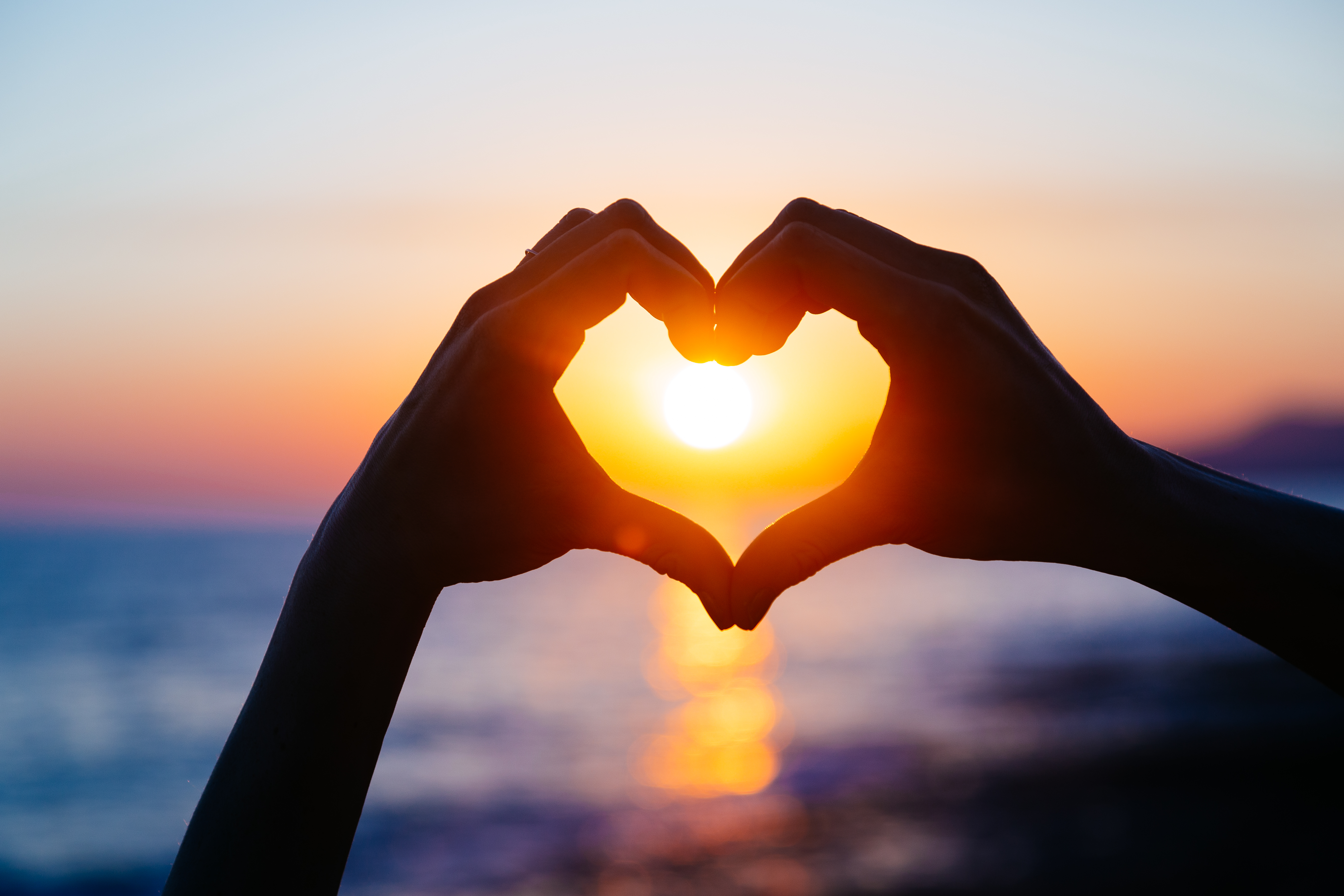 hands forming a heart shape with sunset silhouette