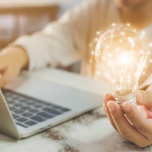 Woman hand holding light bulb and using laptop on wooden desk. Concept new idea with innovation and creativity